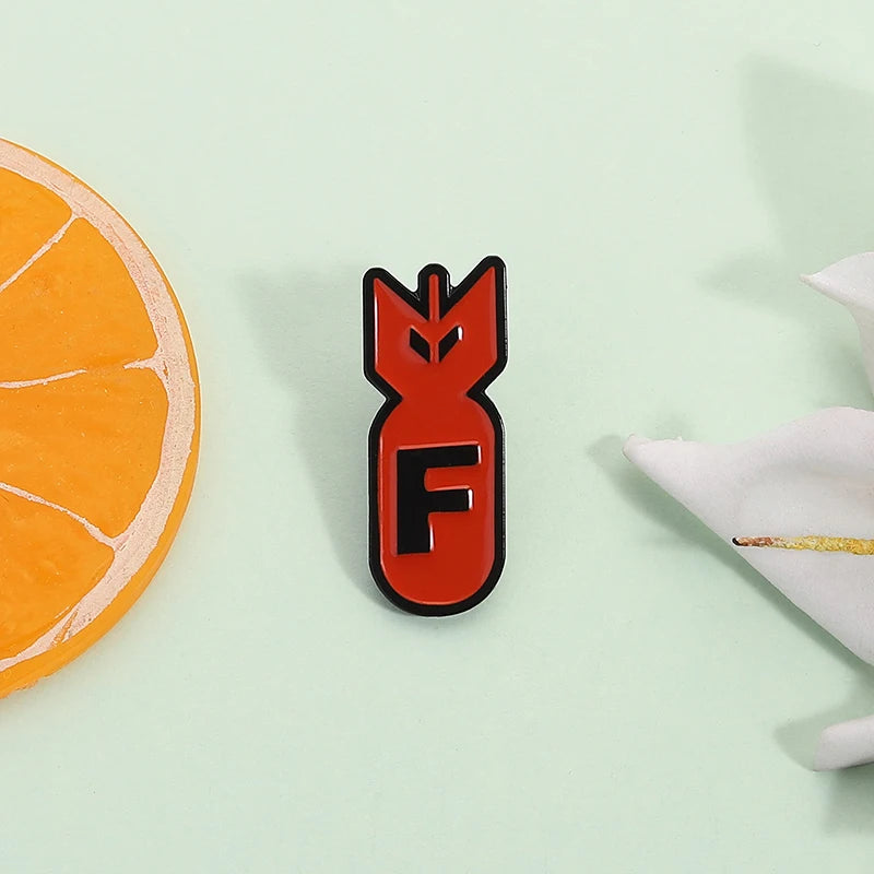 An orange slice and an orange enamel pin featuring a stylized shark design on a light green background.