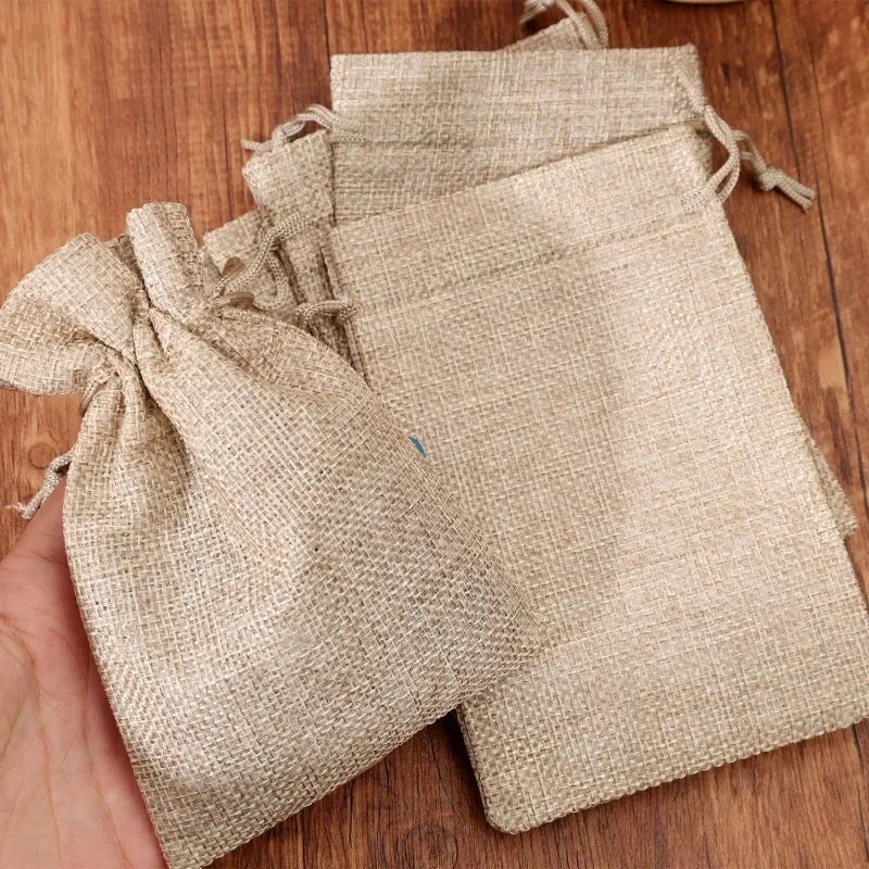 Several natural burlap drawstring bags are shown resting on a wooden surface.