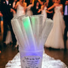 A collection of clear LED foam glow sticks are displayed in a plastic container on a reflective surface.