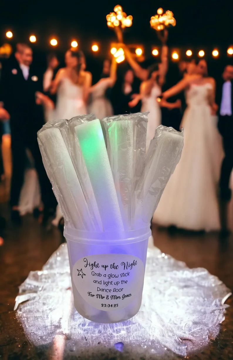 A collection of clear LED foam glow sticks are displayed in a plastic container on a reflective surface.