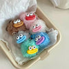 A collection of cute plush sausage-mouth keychains in various pastel colors, including pink, brown, and blue, resting in a li