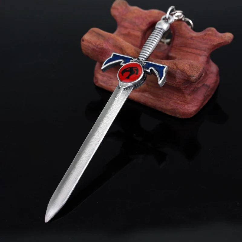 A silver Thundercats metal lion mark sword keychain with a blue and red blade set against a wooden background.