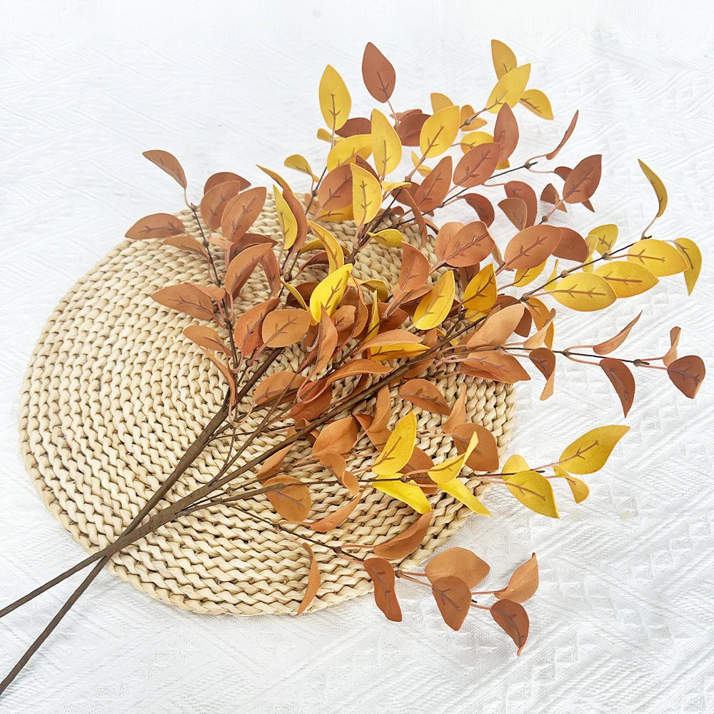 Dried artificial eucalyptus stems in shades of brown and yellow arranged on a woven mat.