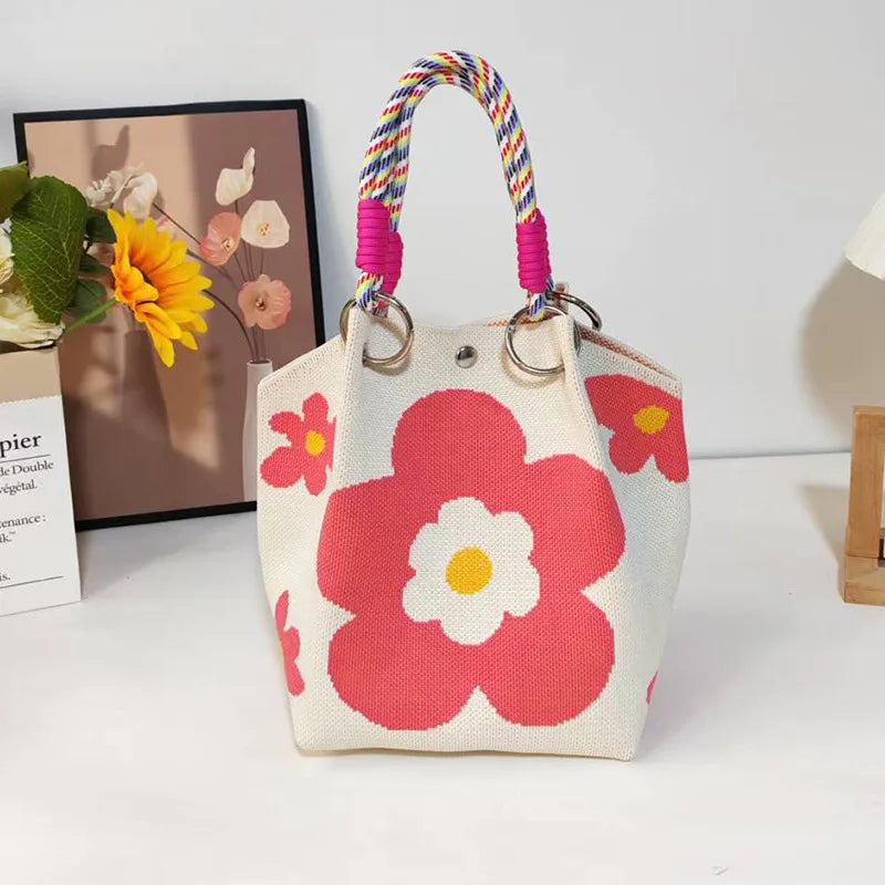 A hand-stitched canvas shoulder bag featuring a pink and white floral pattern with a braided multicolored strap.