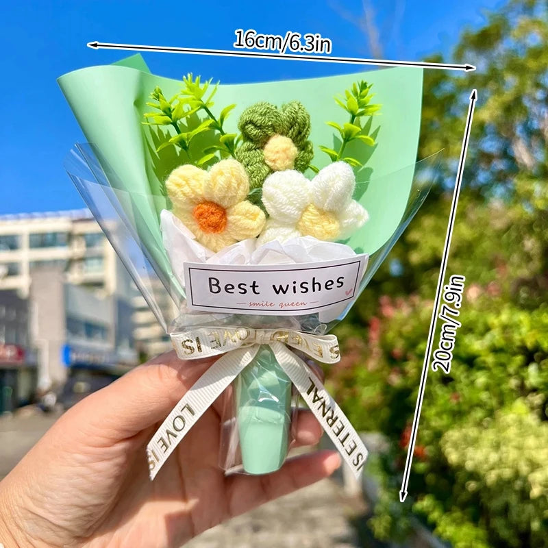 A hand holds a bouquet of handmade crochet flowers in a clear plastic wrap against a bright outdoor background.