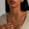A close-up of a woman wearing a gold plated heart pendant necklace on her neck.
