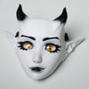 A white fantasy creature mask with black horns and expressive yellow eyes.