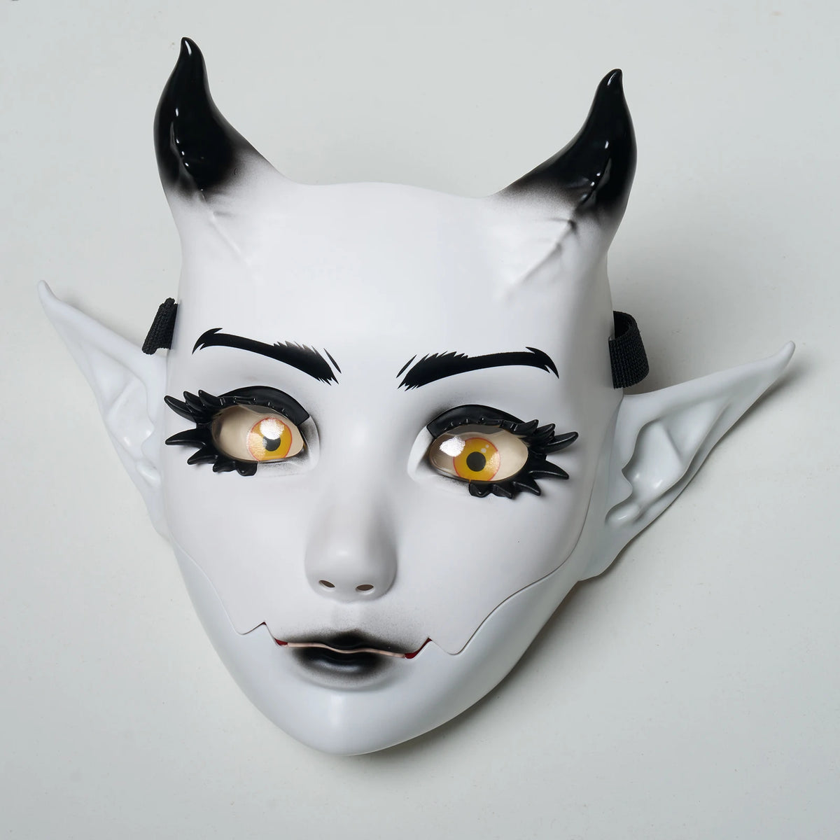 A white fantasy creature mask with black horns and expressive yellow eyes.
