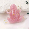 A translucent pink crystal frog resin craft decoration resting on a white surface.