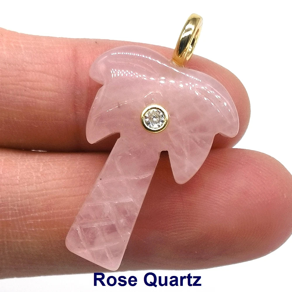 A pink rose quartz crystal pendant with a zircon charm is shown being held by a person's finger.