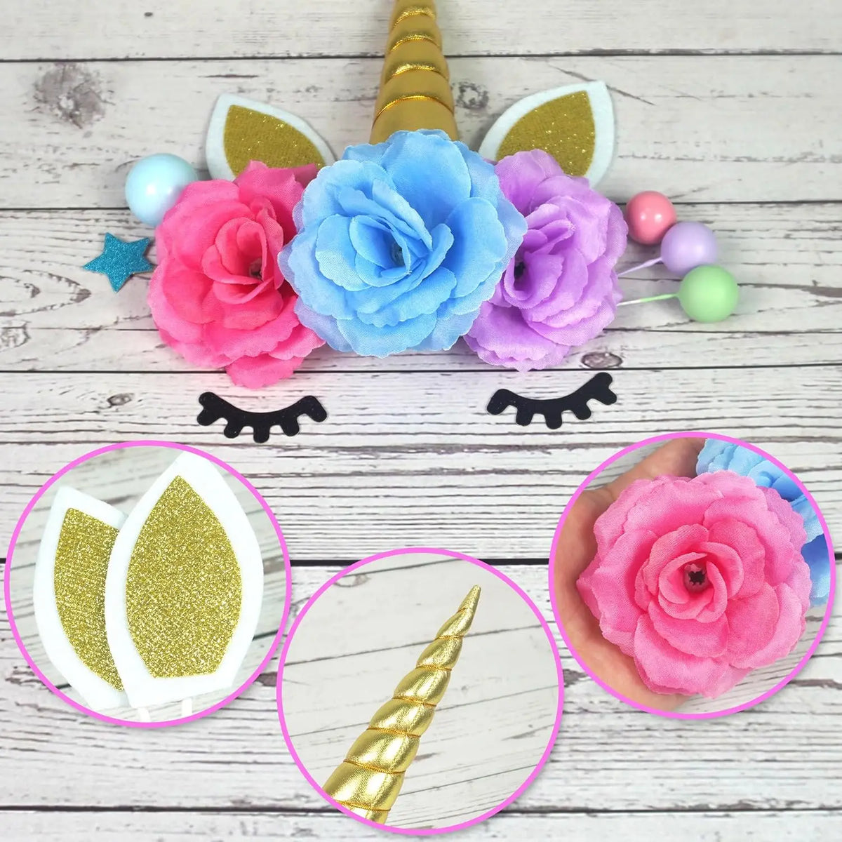 A collection of unicorn cake decorations including pink and blue flowers, gold stars, and colorful balls on a white wooden ba