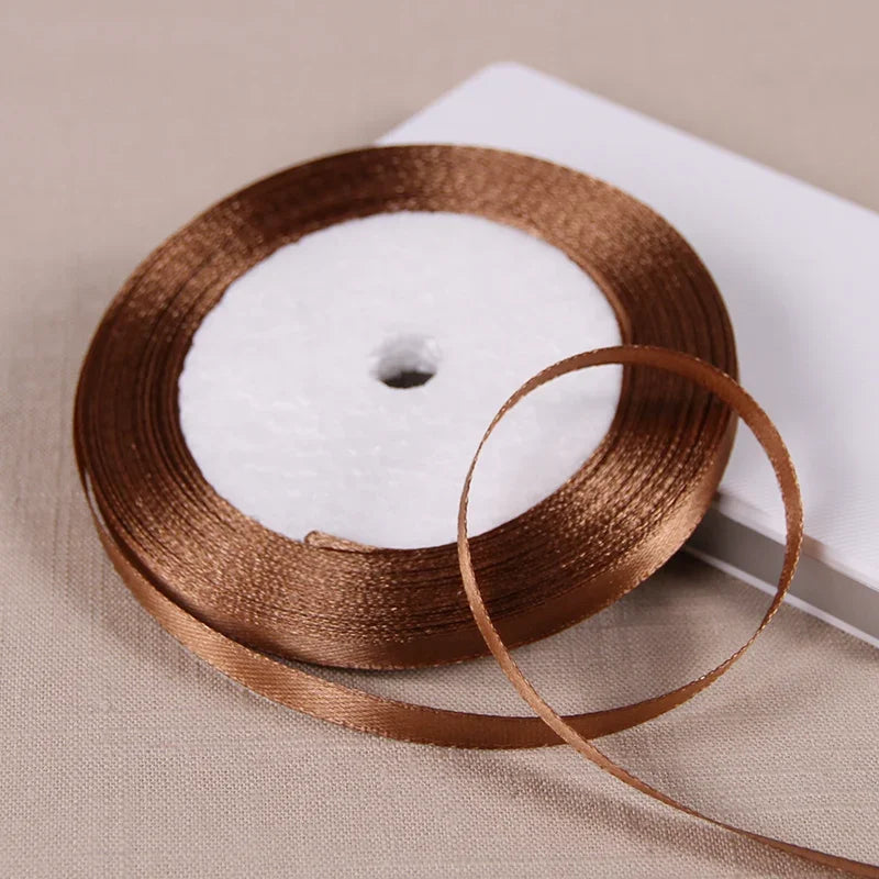 A spool of satin ribbon in a warm bronze color resting on a light surface.