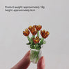 A hand holds a small bouquet of dried orange glass flowers in a clear glass vase.