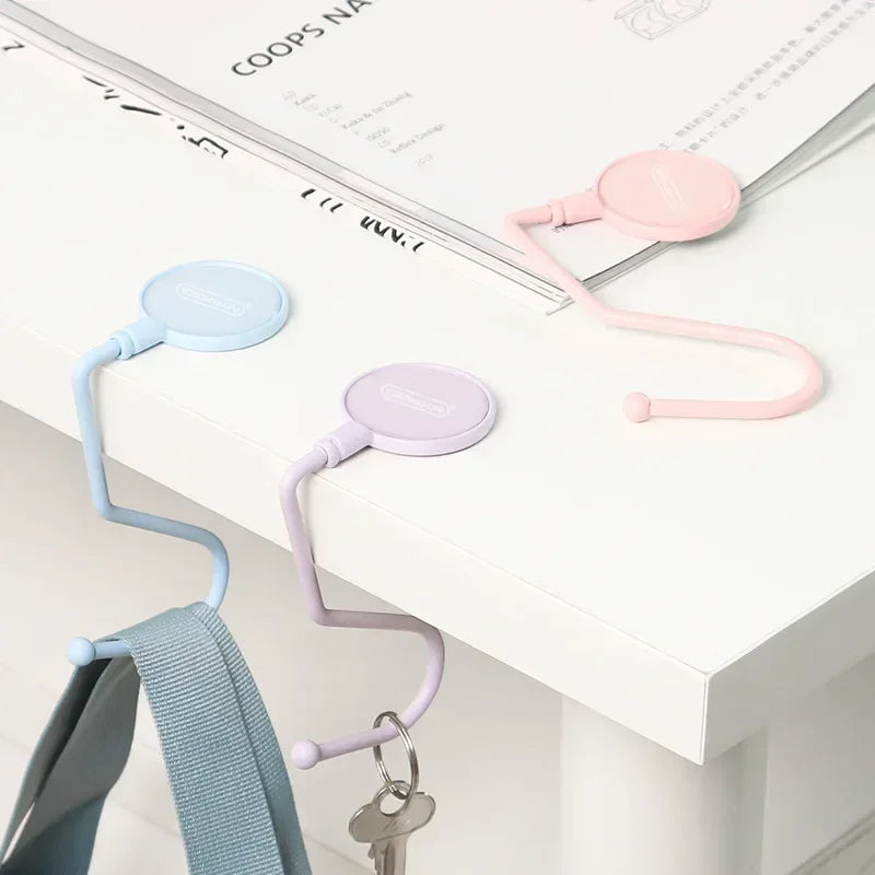 Pink and blue heavy duty purse and bag hooks displayed on a white surface next to a document.