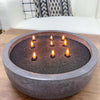 A dark gray ceramic bowl holds several lit candles on a wooden surface.