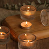 A collection of gold glass tealight candle holders with flickering candles arranged on a wooden tray.