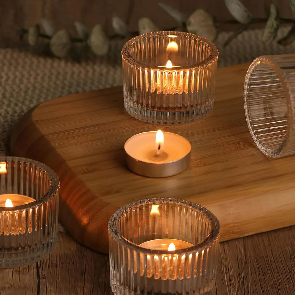A collection of gold glass tealight candle holders with flickering candles arranged on a wooden tray.