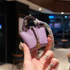 A hand holds a purple mini house handbag with a patterned wrist strap against a dark background.