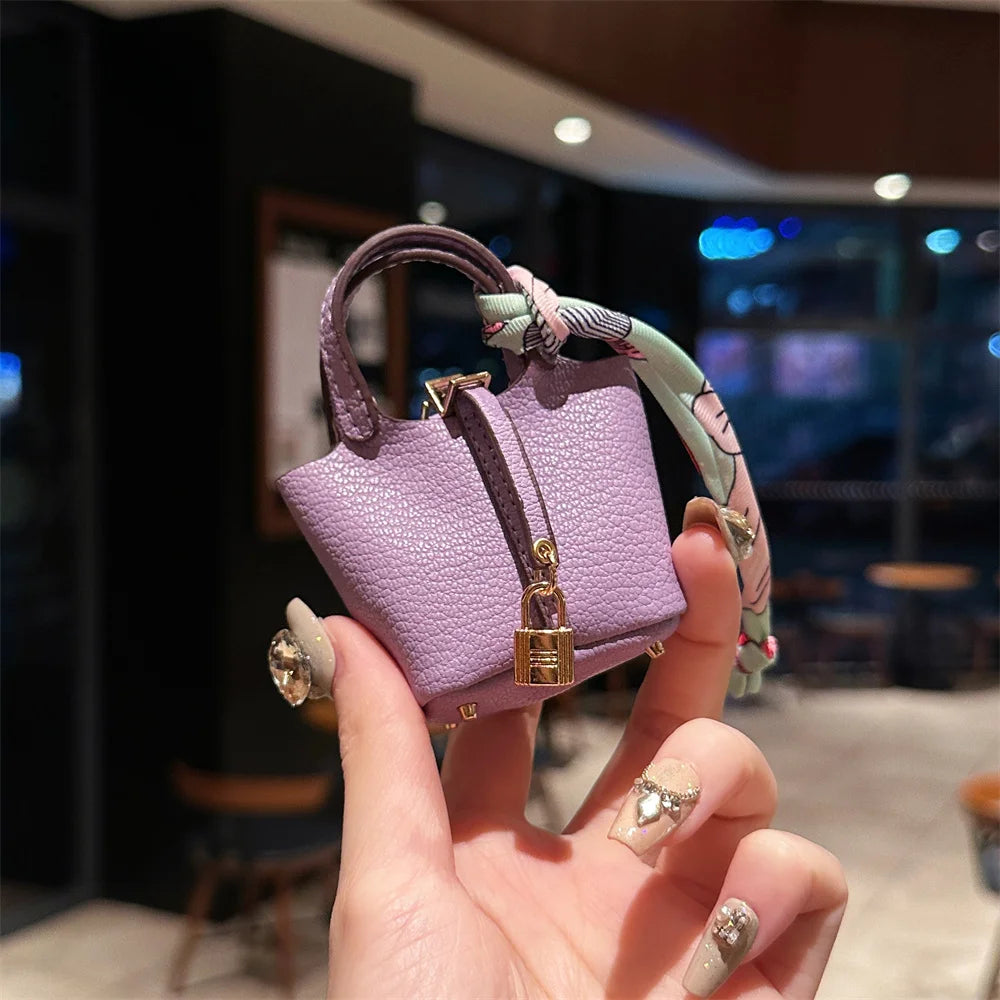 A hand holds a purple mini house handbag with a patterned wrist strap against a dark background.
