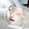 A white masquerade mask with red blood-like markings and a lip design is displayed on white fabric.