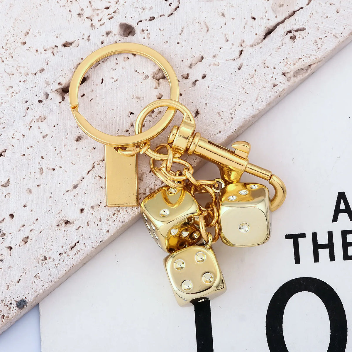 A gold-colored keychain featuring a rectangular charm and several small dice charms.
