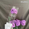 A clear glass vase holds a bouquet of purple crochet tulips with the word LOVE visible on the glass.