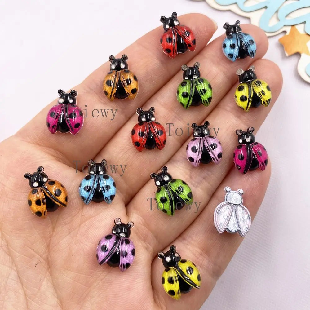 A hand displays various colorful resin beetle rhinestone appliques for DIY crafts.