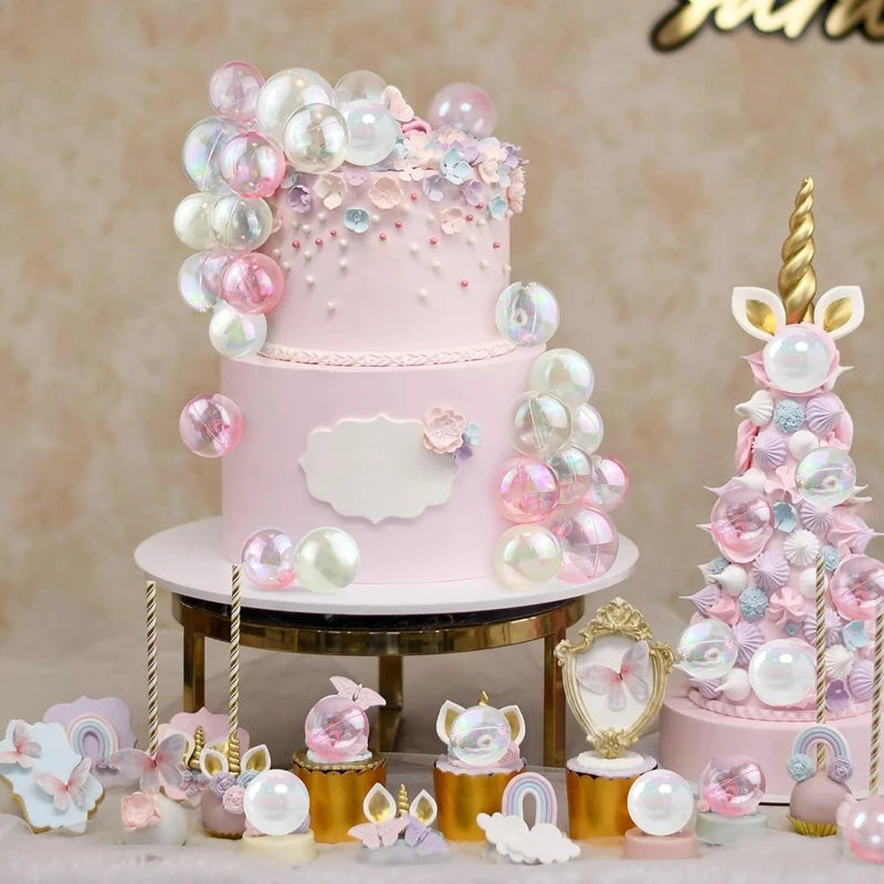 A two-tiered pink cake decorated with clear and pink balloons and floral accents on a gold stand.