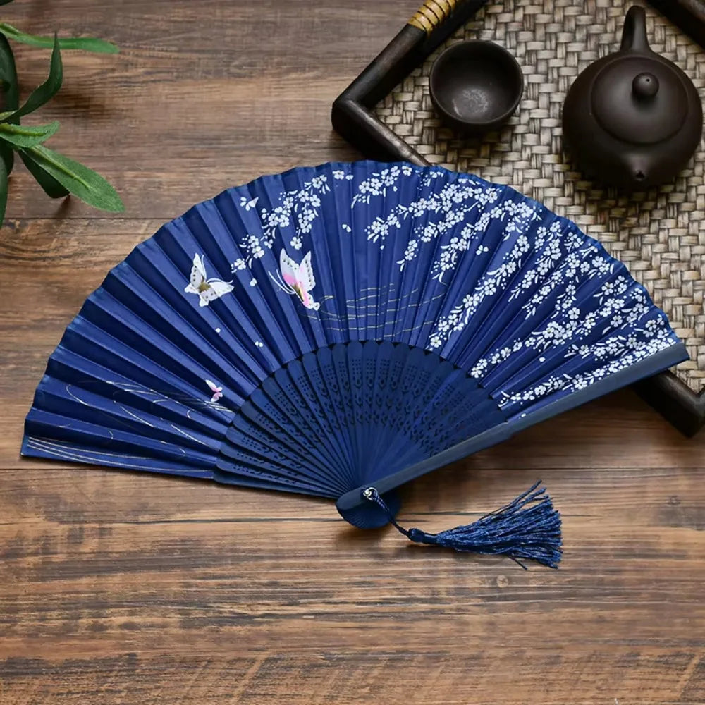 A dark blue antique style bamboo folding hand fan with white floral designs resting on a wooden surface.