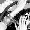 A hand wearing a heavy silver bracelet grips a red steering wheel in a black and white photo.