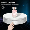 A hand presses a button on a white rotating display stand for jewelry or items.