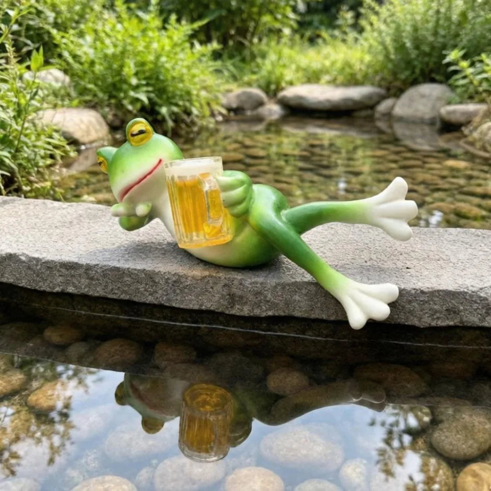 Una figura de rana de resina verde sostiene una copa de cerveza junto a un río claro.