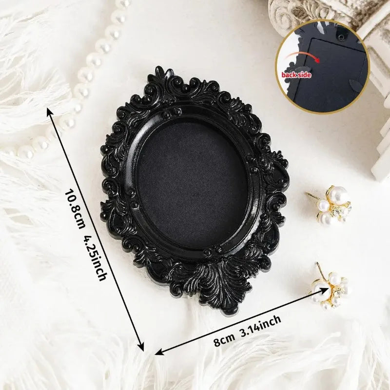 A black vintage resin mini picture frame with an ornate, ruffled edge is displayed on a white, fluffy surface.