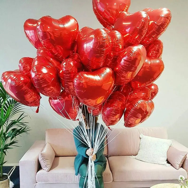 A large bouquet of red heart-shaped foil balloons is displayed in front of a light pink sofa.