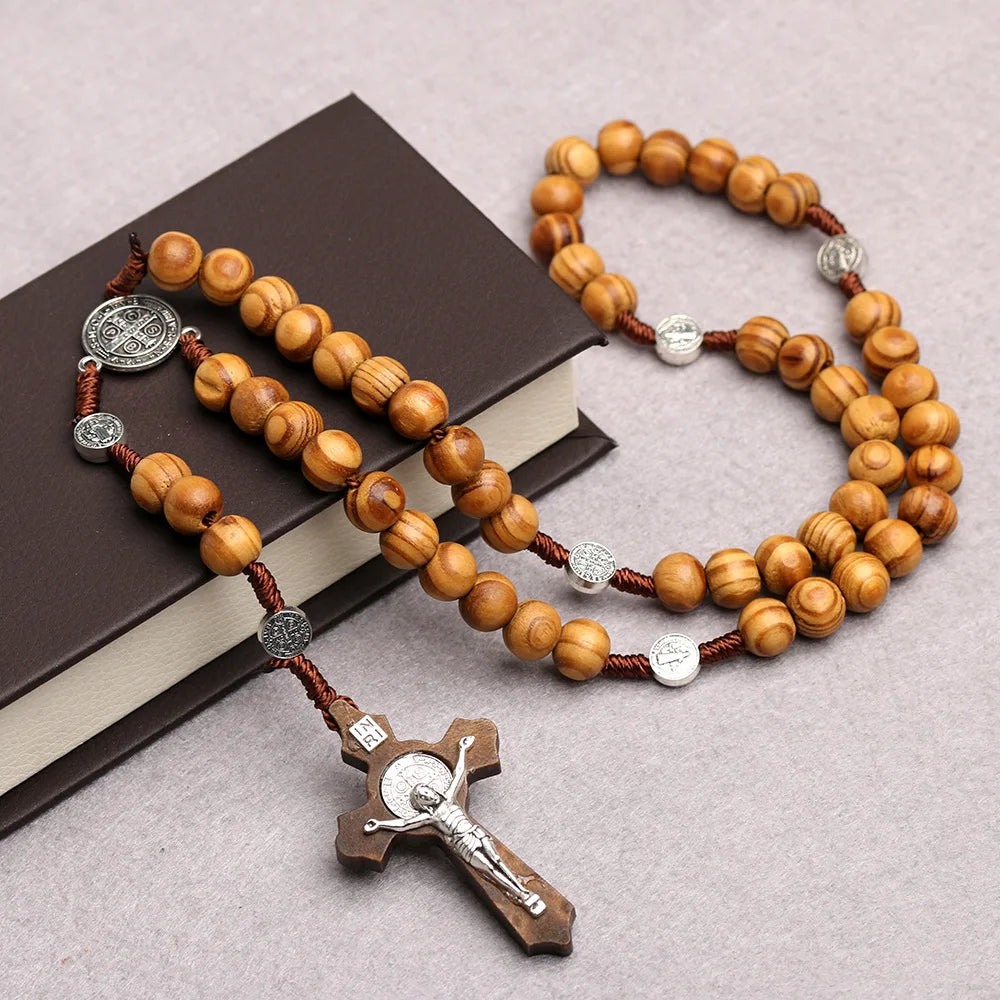 A wooden bead rosary cross necklace with silver accents resting on a dark book.
