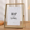 A modern metal photo frame with a gold finish holds a card that reads Keep life simple.