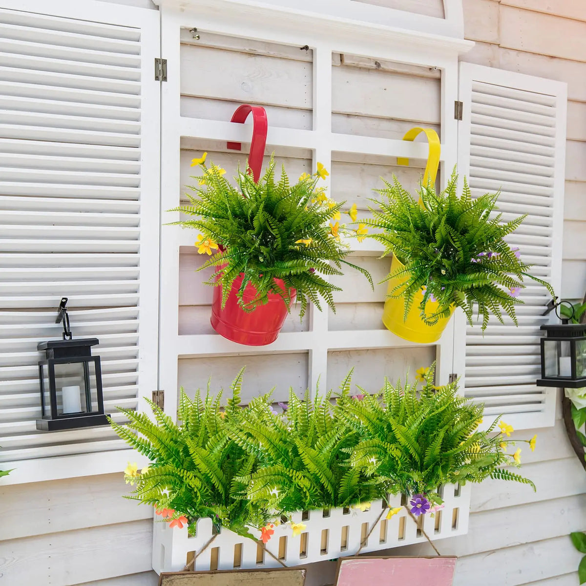A display of artificial green Boston ferns and shrubs in red and yellow pots mounted on a white wooden panel.