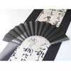 A black glitter folding fan with transparent ribs is displayed against a background of traditional Japanese writing.