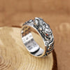 Silver pixiu ring featuring detailed coin designs resting on a wooden surface.