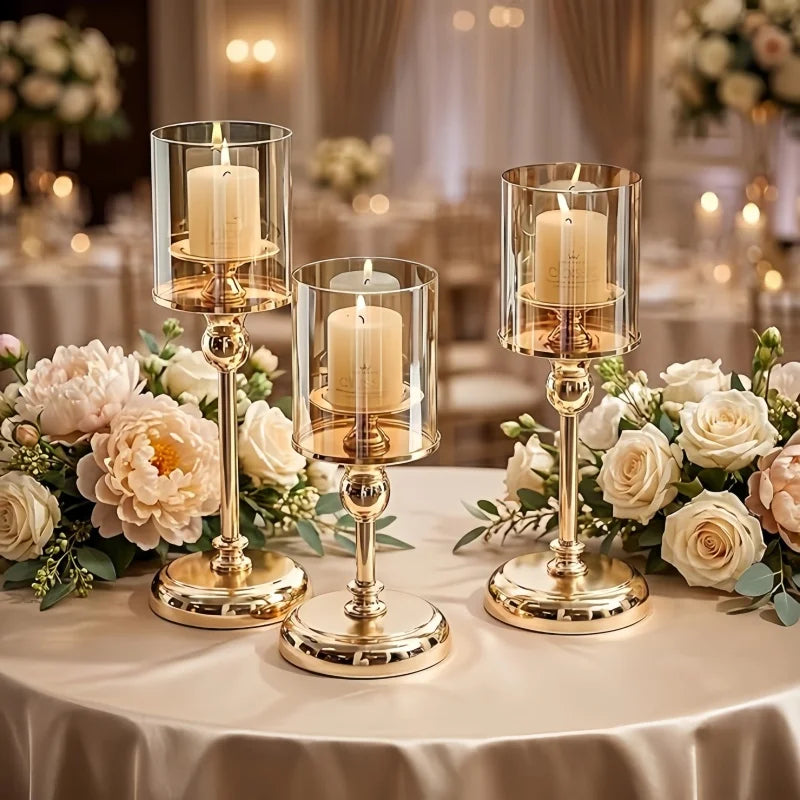A display of four gold-toned metal pillar candle holders on a table decorated with white and blush roses.