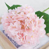 A large bouquet of pink artificial hydrangea flowers displayed on a wooden board.