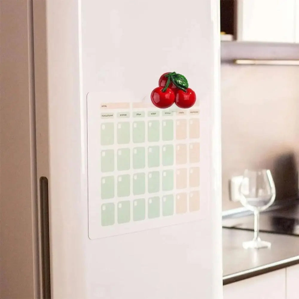 A white refrigerator door features a grid of fruit magnets and a decorative cluster of red apples.