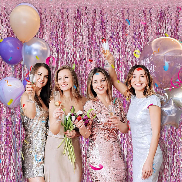 Cinco mujeres posando frente a un fondo de flecos de papel rosa para un evento