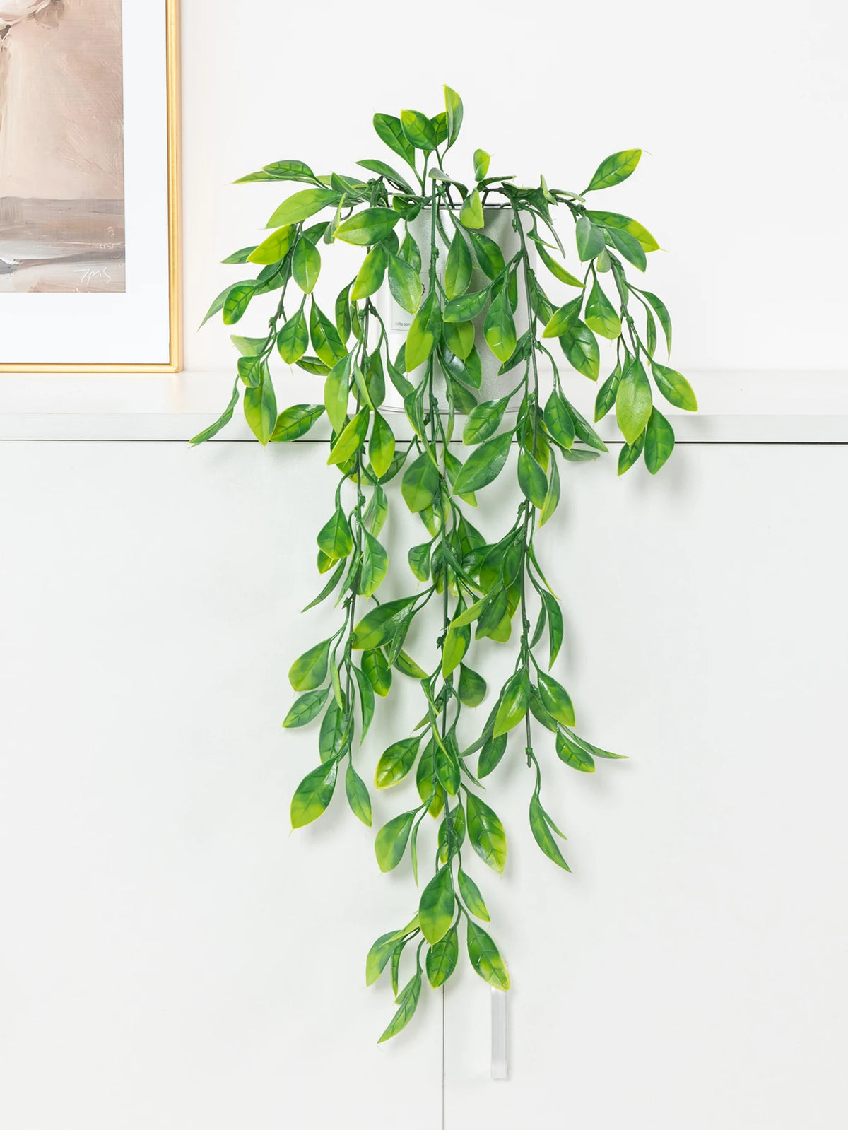 Artificial ivy garland with a pot hanging vertically against a white wall.