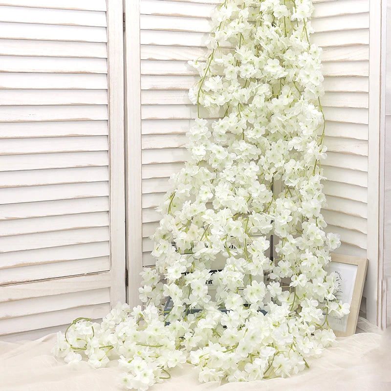 A vertical arrangement of white artificial sakura flowers cascading down, set against a light wooden slatted background.