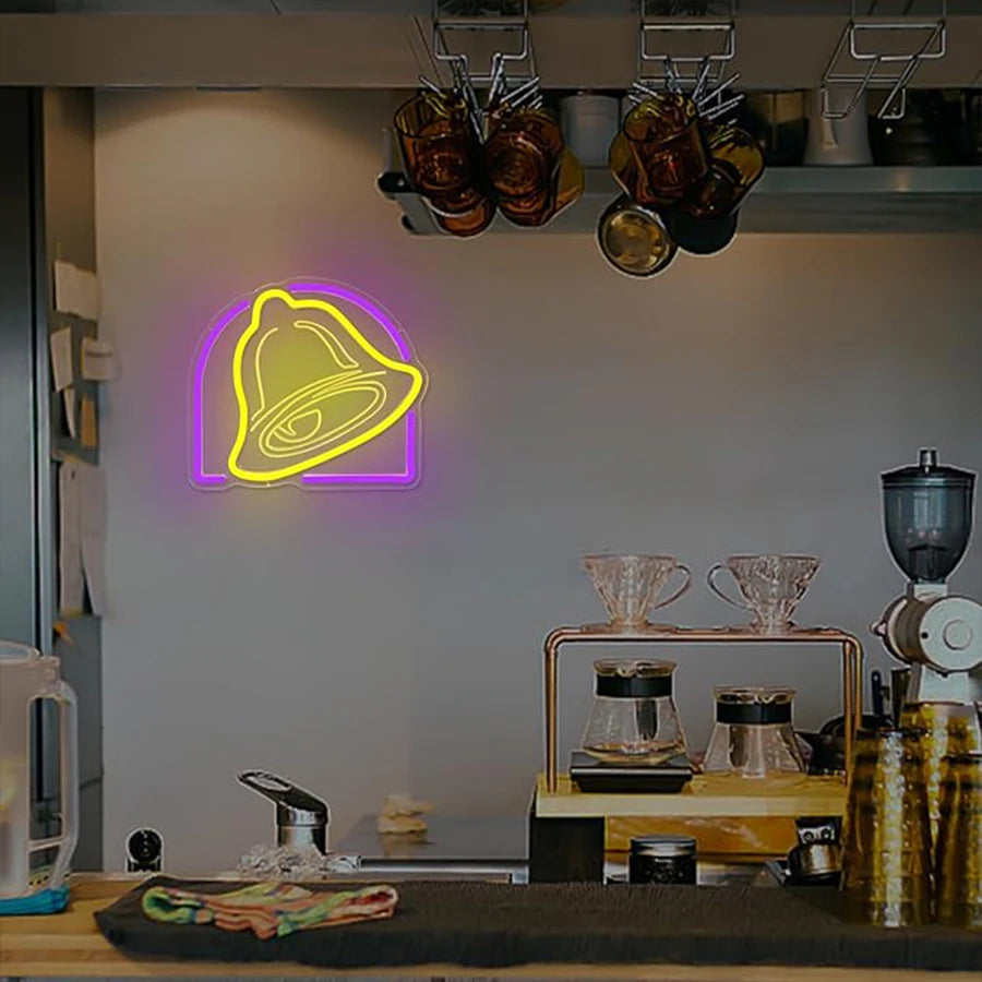A glowing yellow bell-shaped neon sign hangs on a shelf in a kitchen setting.