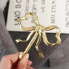 A hand holds an elegant brass bowknot wall hook used for home organization.