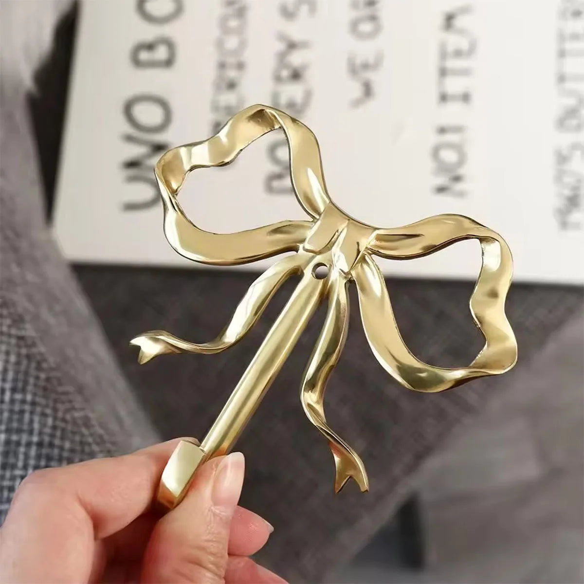 A hand holds an elegant brass bowknot wall hook used for home organization.