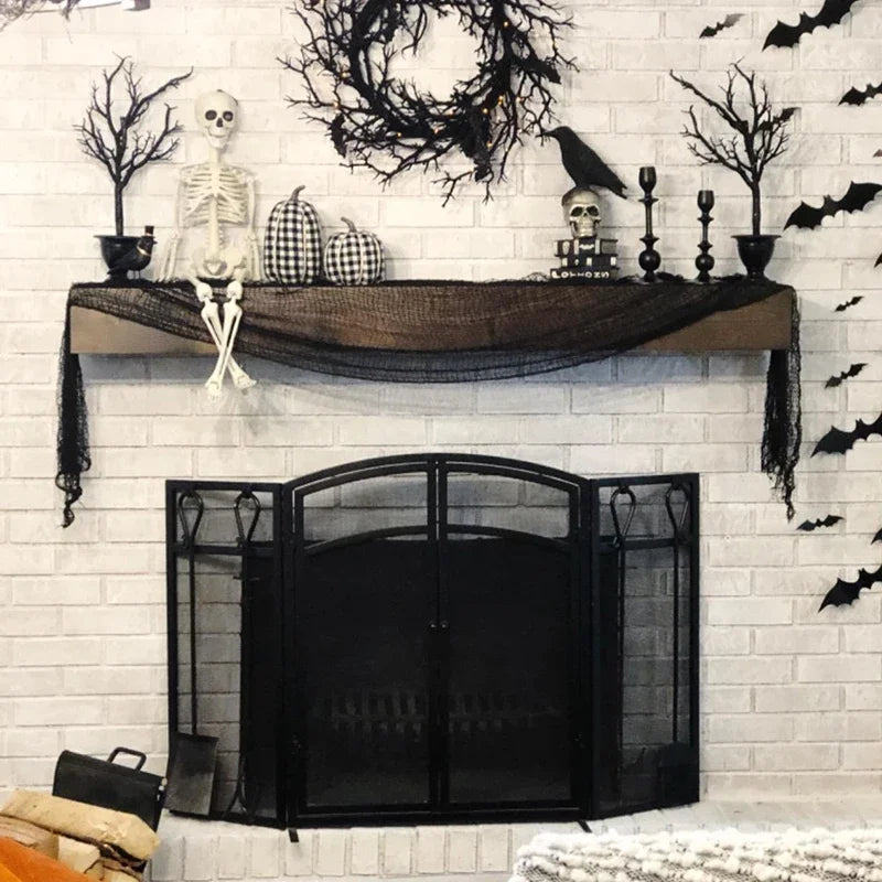 Black Halloween gauze netting draped over a shelf decorated with skulls and branches on a white brick wall