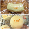 Two squishy toys shaped like banana bears made with a butter texture are packaged in clear plastic.